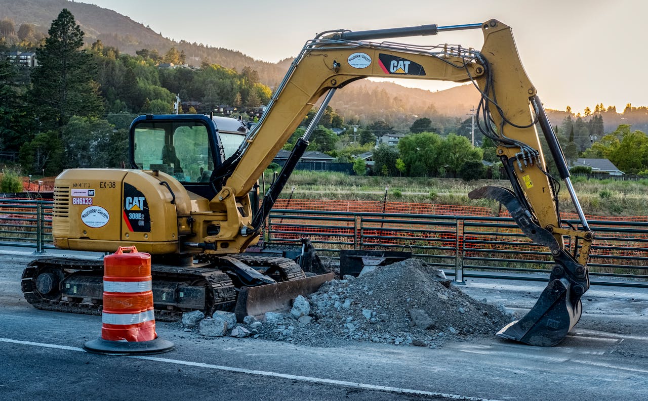 A Caterpillar excavator working on a road construction site with a pile of gravel.