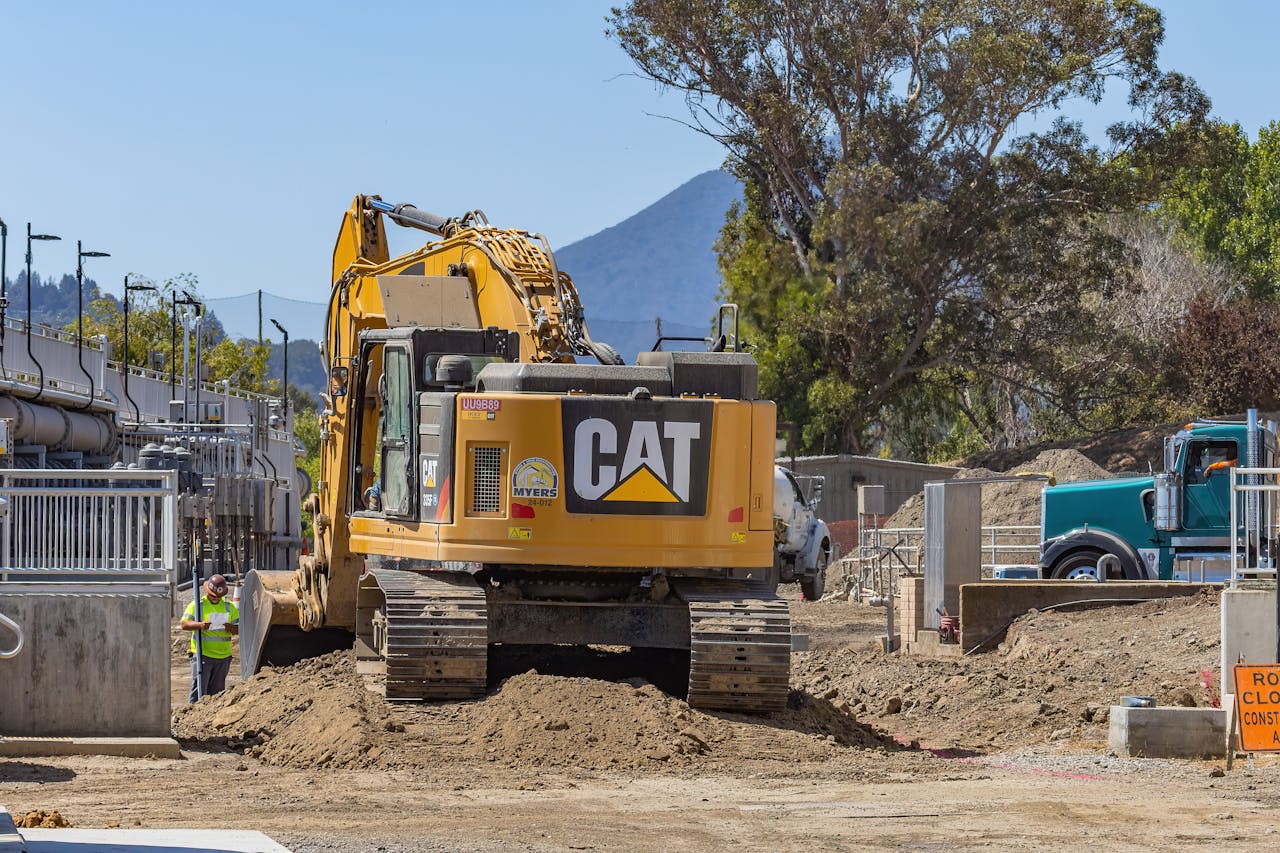 why-choose-us Excavator working at a construction site with mountains in the background.