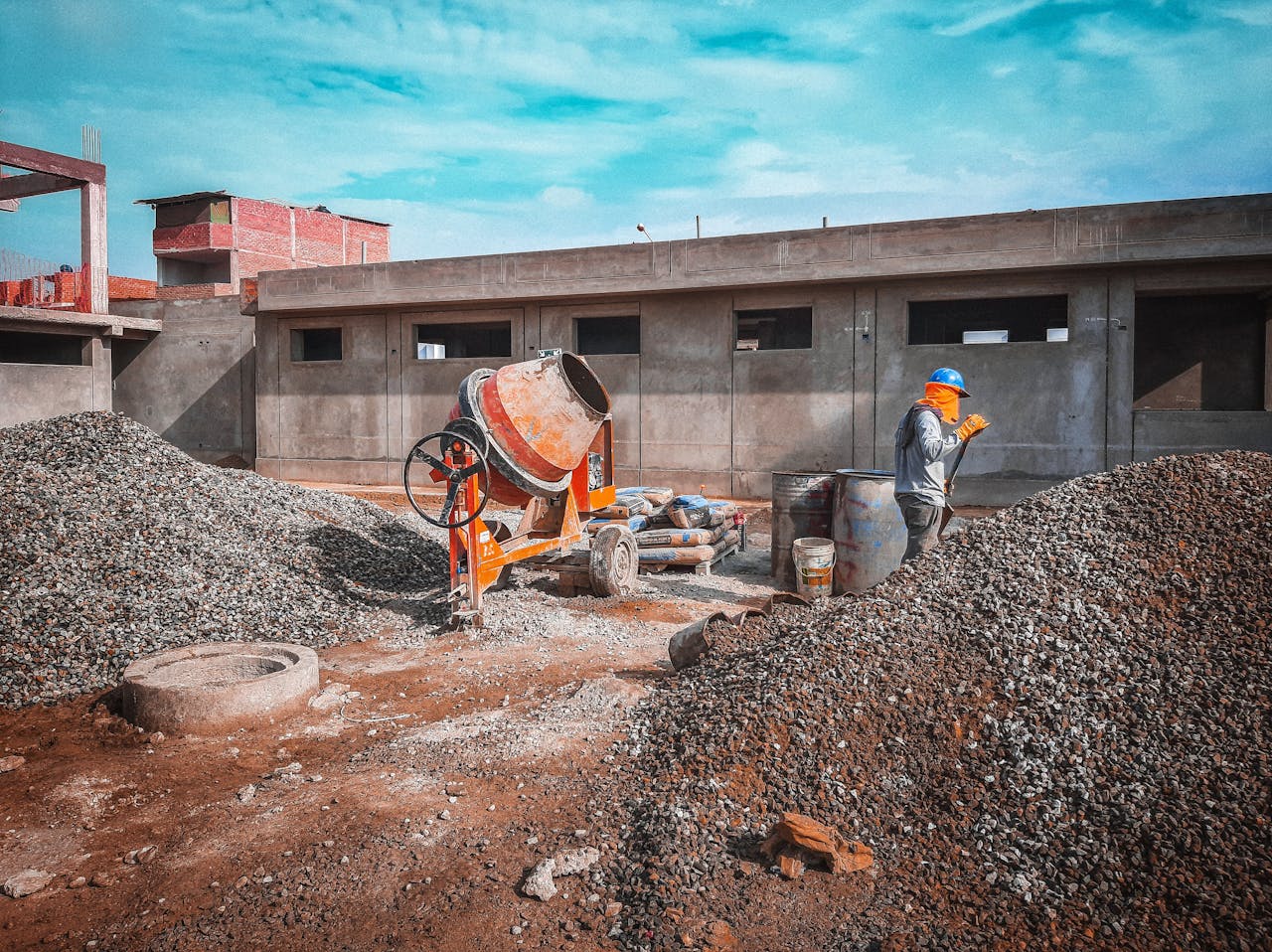 home-hero A construction site with a worker wearing safety gear next to a cement mixer and gravel piles.