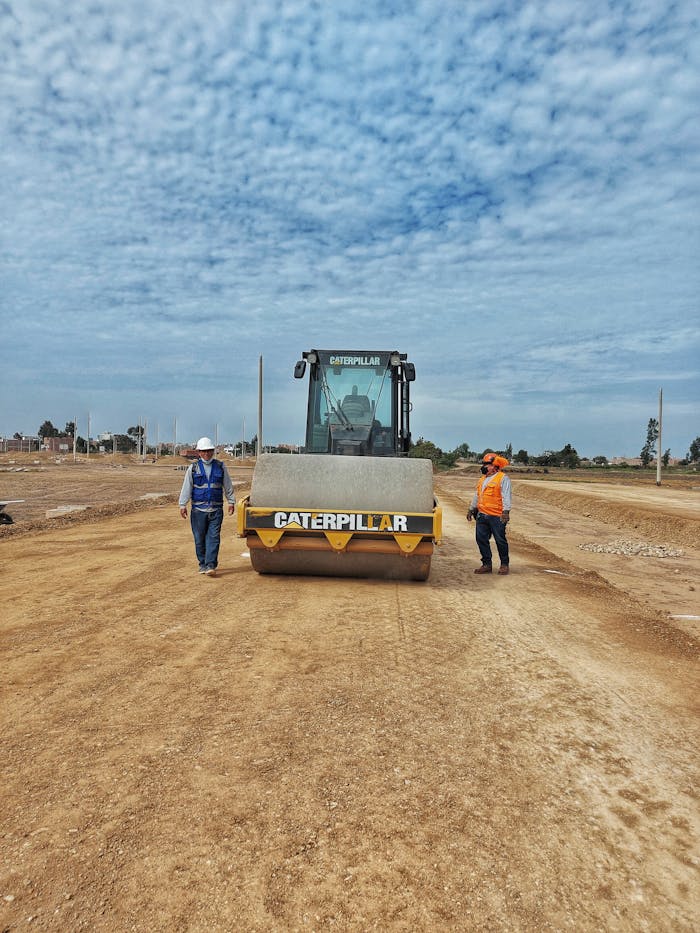 Construction workers with Caterpillar machinery on a dirt road under a cloudy sky.
